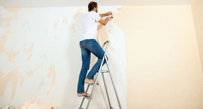 man removing wallpaper on ladder